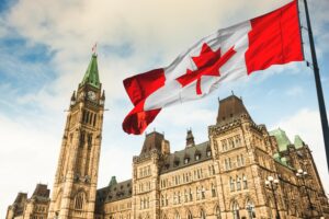 A CANADIAN FLAG FLIES IN FRONT OF A LARGE GOTHIC BUILDING