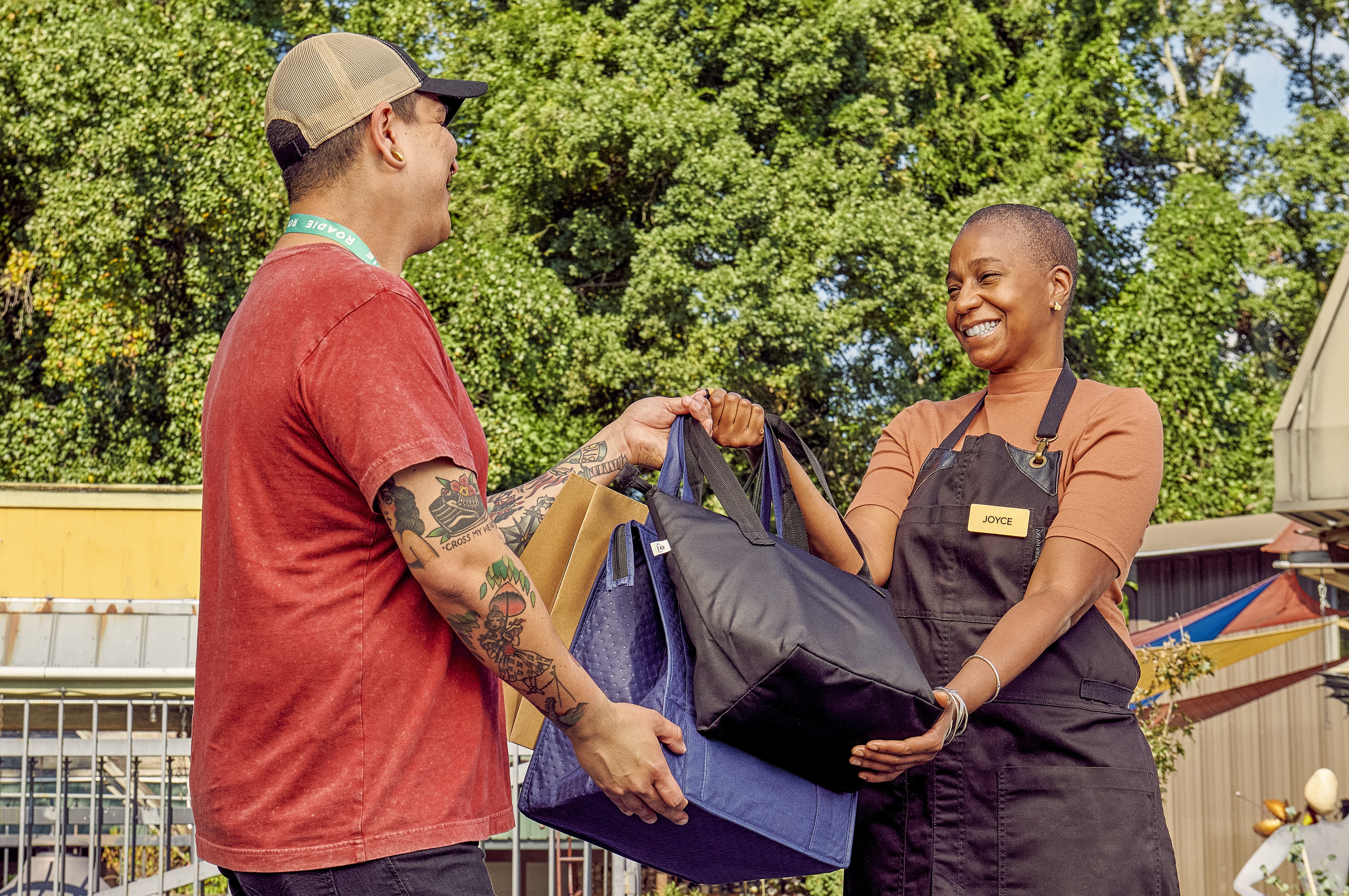 A MAN HANDS A SMILING WOMAN SEVERAL SHOPPING BAGS IN A GARDEN