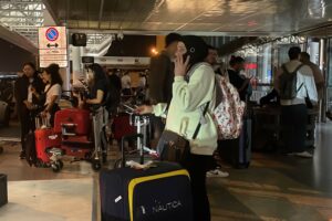 A WOMAN IN A HEAD COVERING ON A MOBILE PHONE STANDS IN A CROWDED AIRPORT LOUNGE