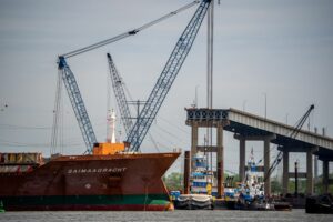 A LARGE SHIP, LABELED Saimaagracht, sails past A DAMAGED BRIDGE STRUCTURE.