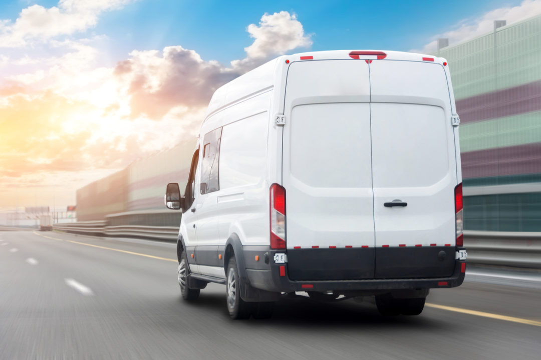 A white minibus delivery truck driving down a road