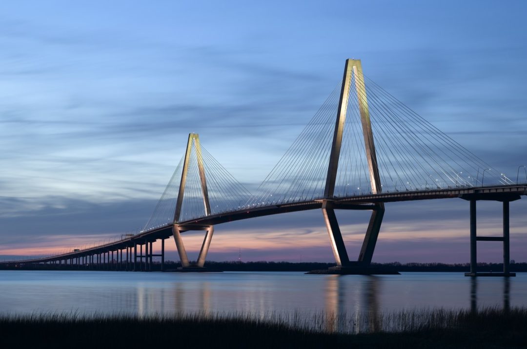 A LARGE, MODERN BRIDGE SPANS A CALM WATERWAY AT DUSK.