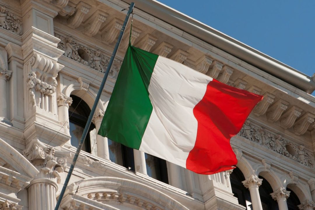 AN ITALIAN FLAG FLIES IN FRONT OF AN ELABORATELY CARVED STONE BUILDING FACADE