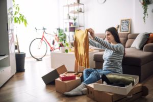 A WOMAN SITTING ON HER LIVING ROOM FLOOR OPENS BOXES OF CLOTHES