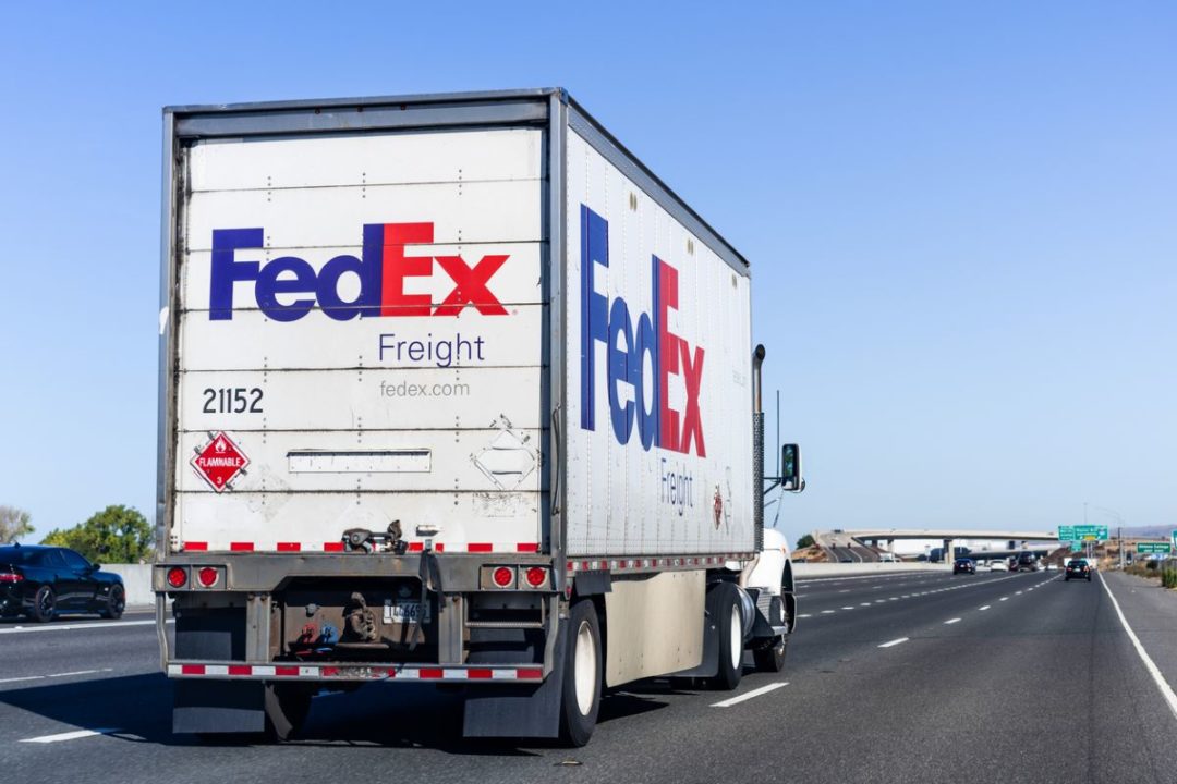 A TRUCK BEARING THE FEDEX FREIGHT LOGO DRIVES DOWN A HIGHWAY UNDER CLEAR BLUE SKIES