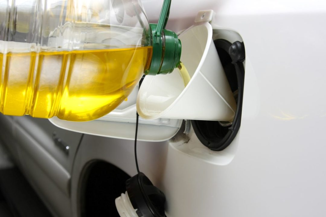 A CLEAR YELLOW OIL IS POURED INTO A CAR'S GAS TANK VIA FUNNEL