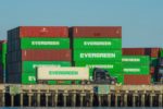 A semi-truck pulling a container next to a stack of other containers at the Port of Los Angeles