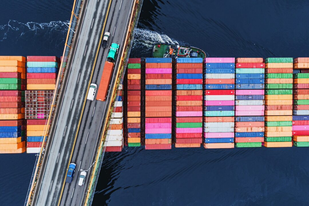 An overhead view of a container ship passing under a roadway