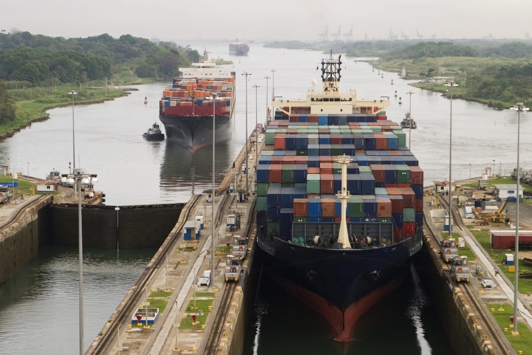 Several freighters, assisted by tugboats, are entering the Panama Canal at Gatun Locks on the Atlantic side. These container ships are fully loaded with cargo heading west towards the Pacific.