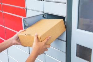 TWO HANDS HOLD A BOX AT THE MOUTH OF AN OPEN LOCKER IN A BANK OF LOCKERS