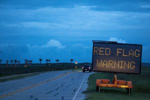 AN ELECTRONIC SIGN READS RED FLAG WARNING NEXT TO A DARK, SOAKED HIGHWAY UNDER BROODING SKIES