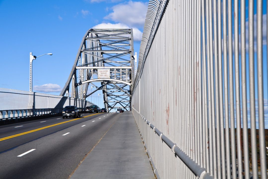 A spanned bridge seen from the road, with cars passing on either side of the roadway