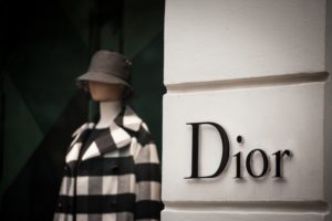 A close-up of a Dior storefront with a mannequin wearing a checkered coat and a hat in the window