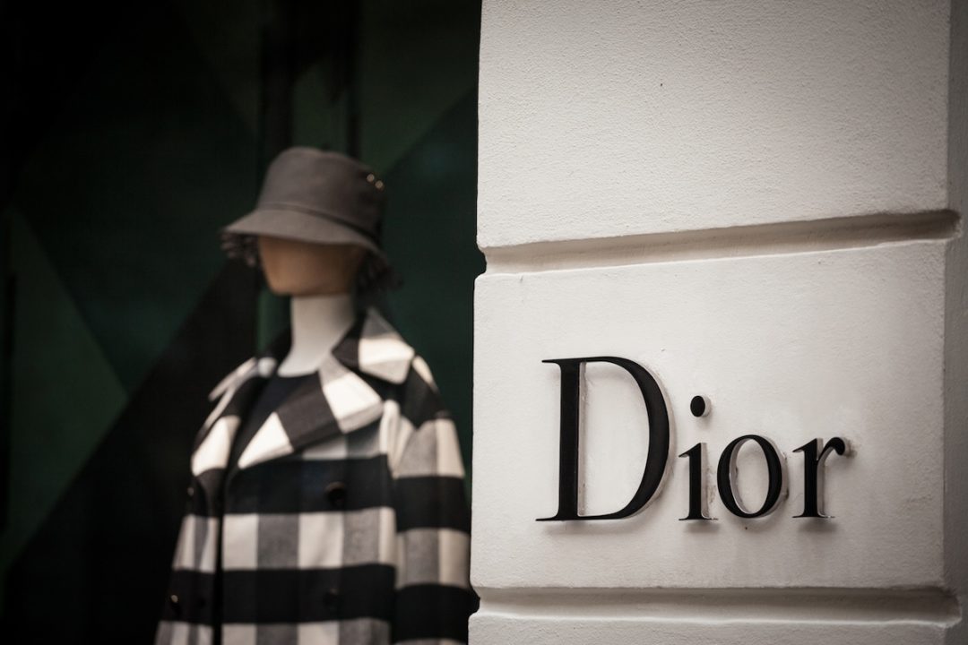 A close-up of a Dior storefront with a mannequin wearing a checkered coat and a hat in the window