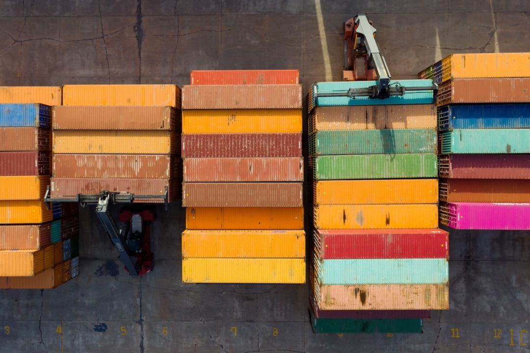 An overhead view of a stack of shipping containers being moved by two cranes on either side