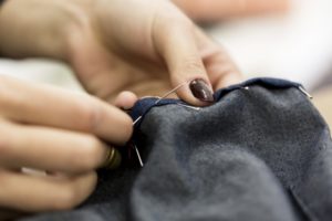 A close-up of hands sewing stitches into an item of clothing