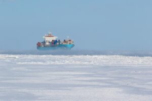 A cargo ship loaded with containers in the distance, moving through an icy, frozen sea