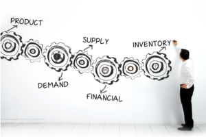 A MAN IN DARK PANTS AND A WHITE SHIRT PEERS AT A GIANT CHART SHOWING COGS REPRESENTING DIFFERENT STAGES OF BUSINESS PLANNING