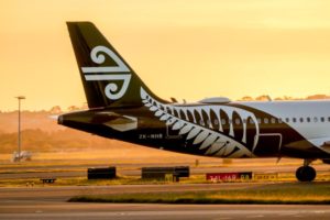 AN AIRPLANE TAIL FIN AND BODY BEARING THE AIR NEW ZEALAND LOGO STANDS AGAINST A SUNSET