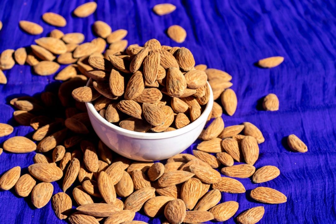 ALMONDS LIE SCATTERED ON A DEEP BLUE BACKGROUND