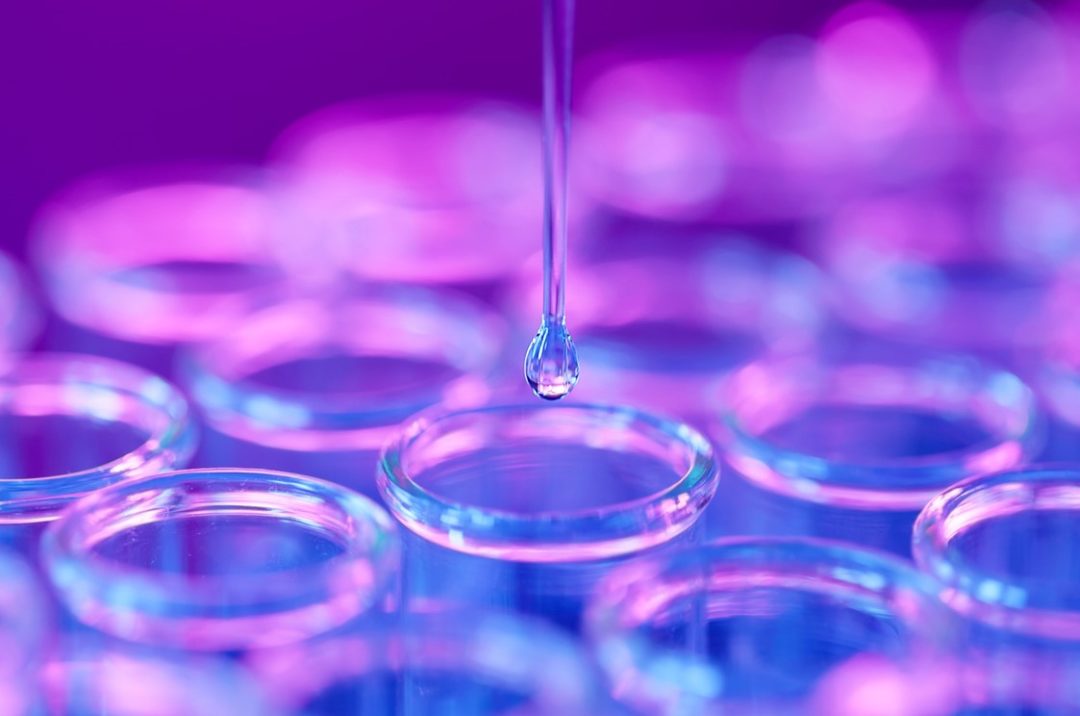 A DROP OF LIQUID FALLS INTO ONE OF A CLUSTER OF TEST TUBES