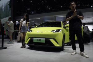 A yellow electric vehicle with a BYD logo on the hood, in a showroom with a man dressed in black standing in front of it