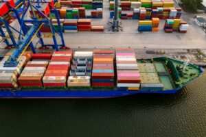 A LARGE CONTAINER SHIP, SEEN FROM ABOVE, IS LOADED WITH MULTI-COLORED CONTAINERS AT DOCK