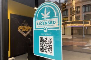 A blue sign on a shopfront that reads "New York State Licensed Cannabis Dispensary" above a large QR code