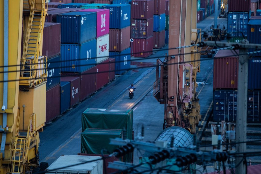 Stacks of shipping containers, with a man on a moped riding through an open space in between stacks