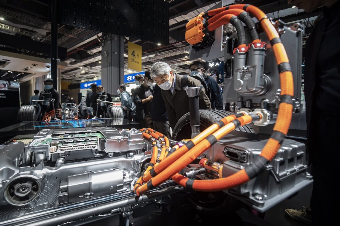 An electric vehicle battery on an assembly line, surrounded by orange cables