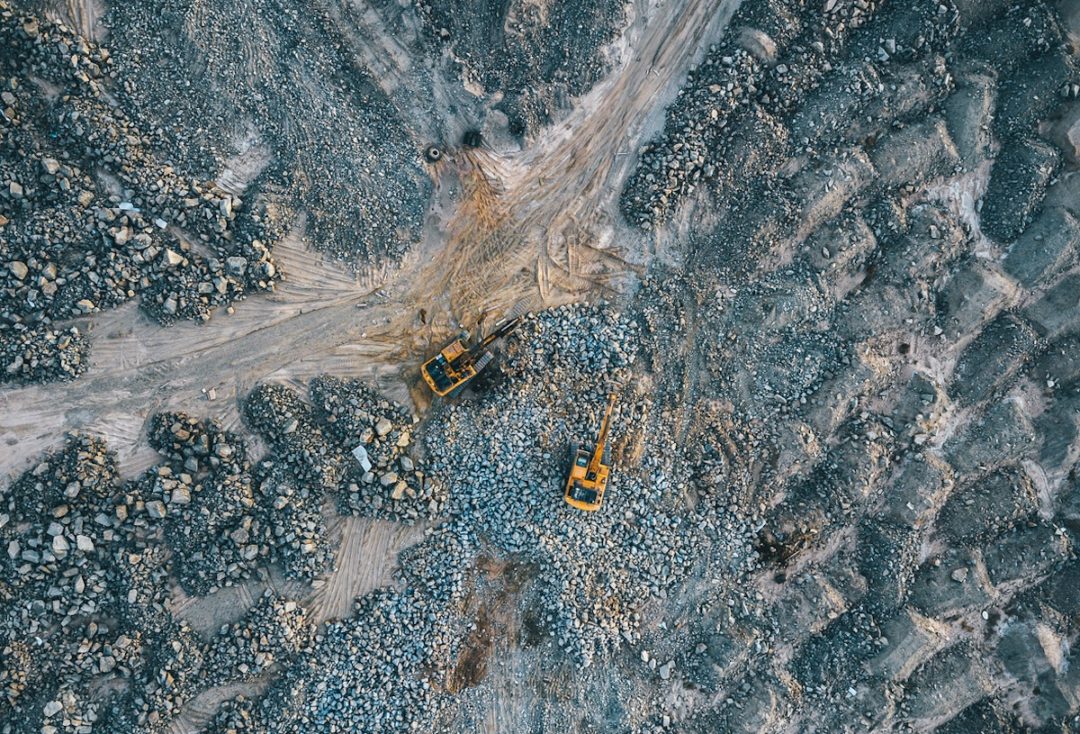 An overhead view of two yellow excavators moving through rocky terrain