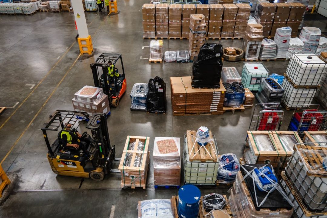 A BIRD'S EYE VIEW OF A BUSY WAREHOUSE, WITH GOODS ON PALLETS AND FORKLIFT TRUCKS