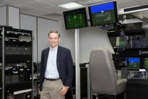 A MAN IN A NAVY BLAZER AND TAN SLACKS STANDS IN A COMPUTER ROOM