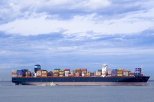 A side view of a large navy blue container ship at sea carrying stacks of containers