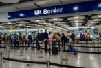 A line of travelers at an airport below a large blue sign reading "UK Border"