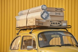 Boxes of Ikea furniture stacked on top of a yellow car in front of a yellow building