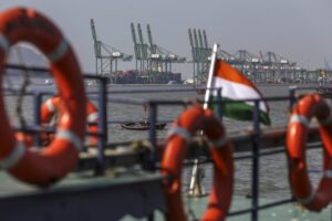 A wide view of three large cranes at a shipping port, with a row of orange life preservers along a rail in the foreground