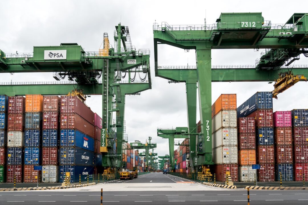 Stacks of shipping containers beside a row of tall green cranes