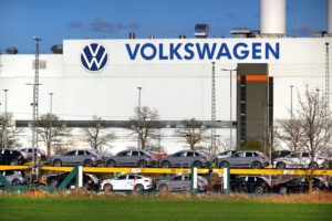 A large white industrial building with the Volkswagen logo on the outside, with a row of cars parked directly outside