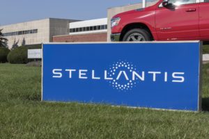 A blue sign reading "Stellantis" in front of a red car and a large grey and white building