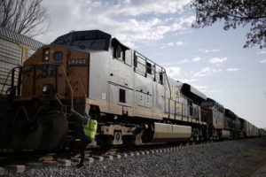 A forward-facing view of a large black and yellow freight train, with a man in a yellow vest climbing onto the front