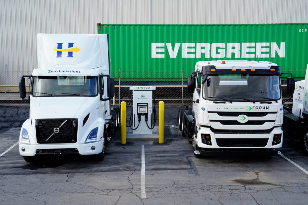 Two semi-trucks, with one pulling a large green trailer with "Evergreen" written in white letters along the side