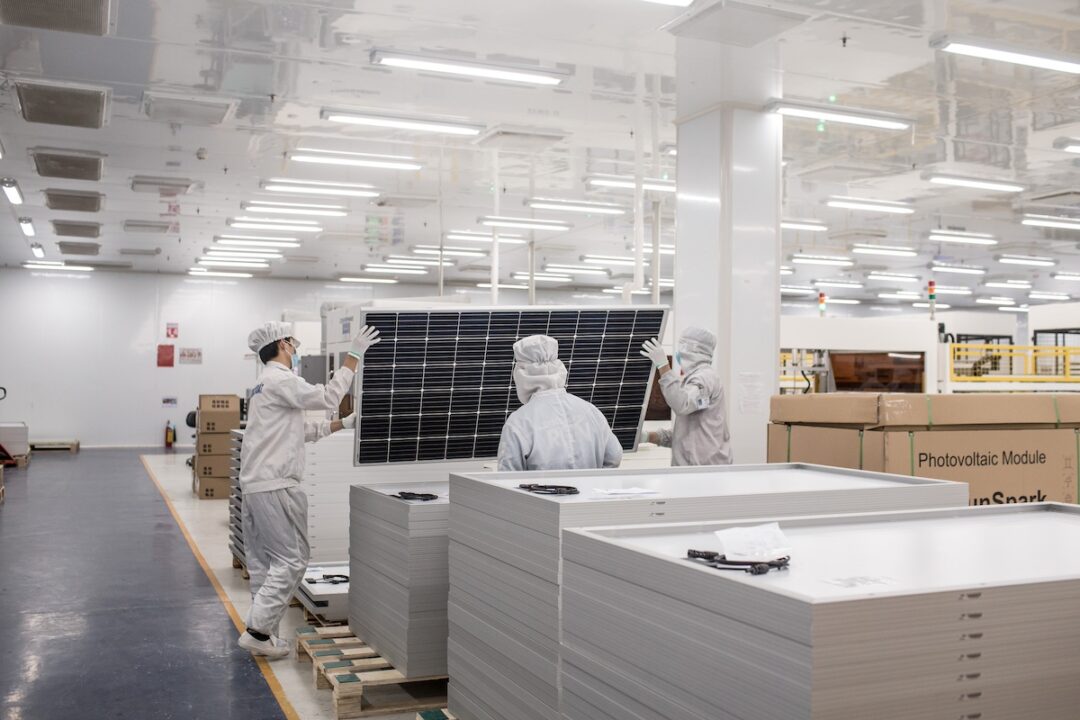 A man in a white clean room suit inside a white manufacturing building lifts a large black panel