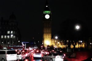 RAIN-SLICKED TRAFFIC AT NIGHT UNDER THE GLOWING FACE OF LONDON'S BIG BEN CLOCK