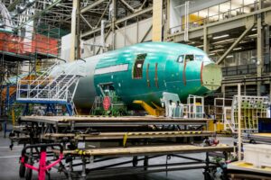 A LARGE GREEN PLANE IS UNDER CONSTRUCTION IN A GIANT HANGAR