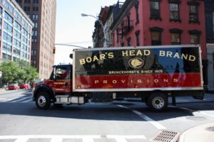 A TRUCK MAKES ITS WAY DOWN AN INNER-CITY STREET, BEARING THE BOAR'S HEAD LOGO, INCLUDING A PICTURE OF A BOAR'S HEAD