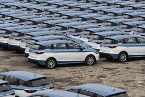 A lot filled with rows of small blue and white hatchback cars. 