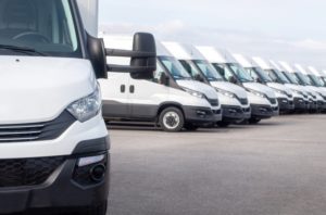 A row of white, unmarked delivery vans, with one of the vans in the foreground facing the camera