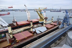 Two blue container ships docked directly next to each other, each carrying stacks of red shipping containers