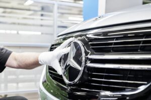 A GLOVED WORKER'S HAND FITS THE MERCEDES-BENZ INSIGNIA INTO A CAR'S SHINY FRONT GRILLE